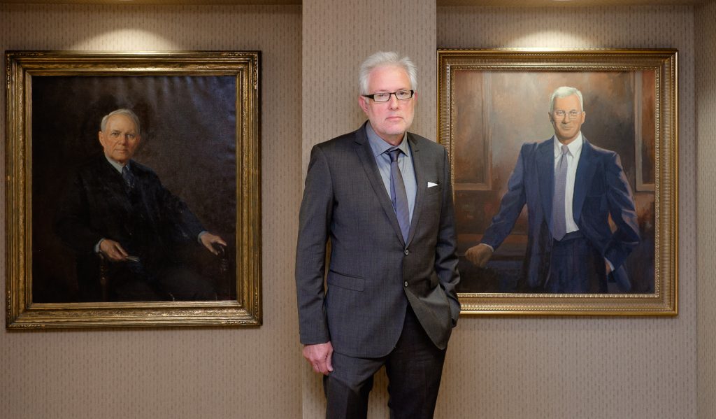 Kristoffer Hellum poses with portraits of Dr. Hans Christian Midelfart, and his son, Dr. Peter Midelfort, at Mayo Clinic Health System in Eau Claire. 